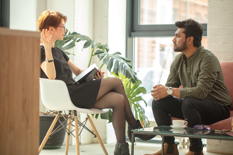 Two people engaged in a conversation while seated in a modern office space, with a coffee table between them.